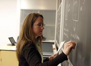 A photograph shows a female teacher writing on a chalkboard.