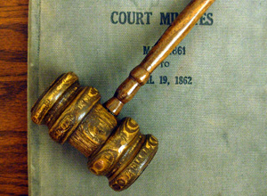 A top-down photograph shows a judge’s wooden gavel lying on top of a court record-keeping book.