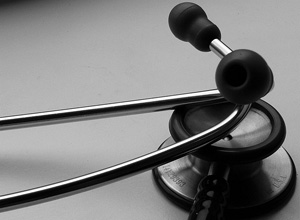 A photograph shows a medical stethoscope lying on a grey surface.